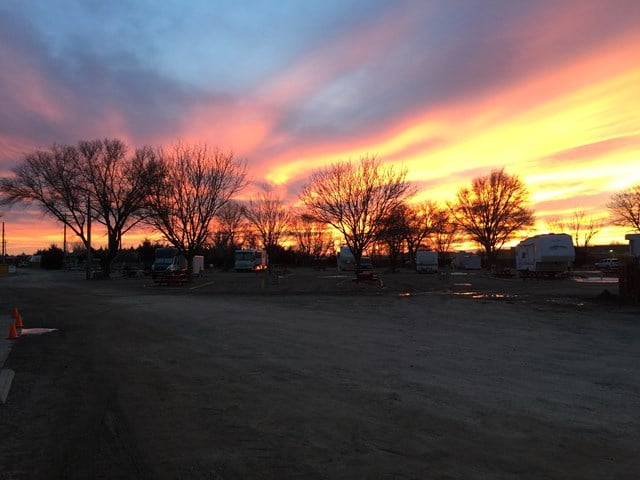 A campground with parked RVs and bare trees at sunset, with a dramatic sky filled with orange, pink, and purple clouds.